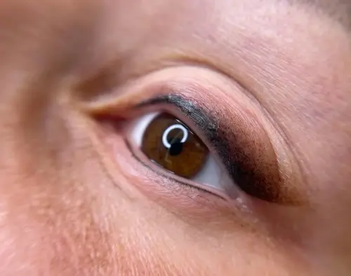 micropigmentacion Primer plano del ojo marrón de una persona con delineador visible en el párpado superior, realzado mediante micropigmentación. La piel alrededor del ojo presenta una textura ligera y variaciones de color naturales. Se aprecia un pequeño reflejo en la superficie del ojo, que muestra los detalles de la reconstrucción. Monica Aranguez