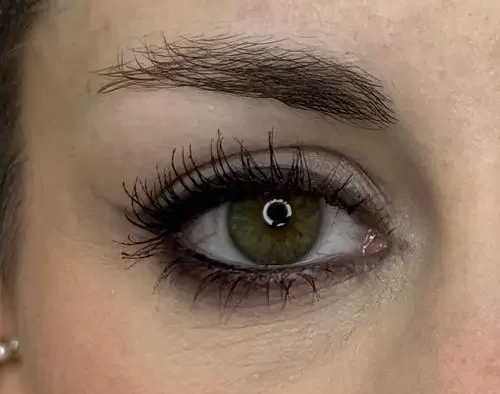 micropigmentacion Primer plano de un ojo verde con pestañas largas y una ceja bien cuidada, realzada con micropigmentación. La piel es clara, con un maquillaje sutil con delineador oscuro y rímel. Monica Aranguez