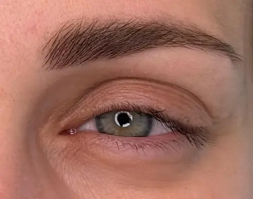 micropigmentacion Primer plano de un ojo verde con maquillaje natural, con micropigmentación de cejas para unas cejas impecables. Las sutiles ojeras muestran la textura natural de la piel, y las pestañas cortas permanecen sin tratamiento. Monica Aranguez