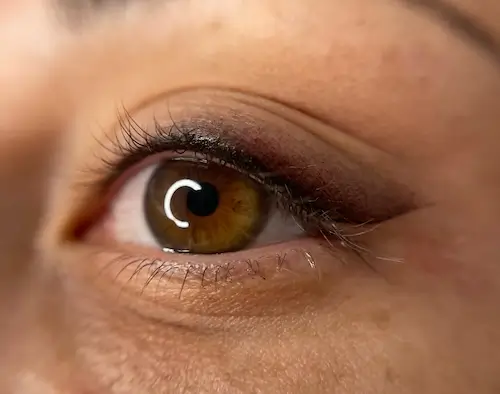 micropigmentacion Primer plano de un ojo humano con iris color avellana, pestañas largas, maquillaje sutil y signos de micropigmentación ocular. La piel del contorno del ojo muestra una textura natural y líneas tenues. Monica Aranguez