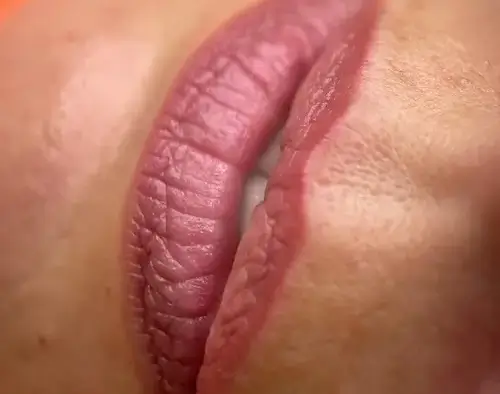 micropigmentacion Primer plano de los labios de una mujer con un labial rosa rojizo, que muestra el arte de la micropigmentación. Los labios están ligeramente separados, dejando entrever los dientes, mientras que la piel circundante permanece impecablemente suave. Monica Aranguez