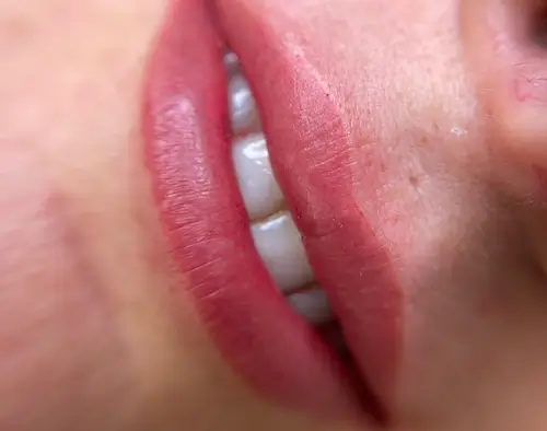 micropigmentacion Primer plano de la boca de una persona que muestra unos labios rosados ligeramente separados, revelando dientes blancos. La piel alrededor de la boca realza la textura y los detalles naturales, mostrando el efecto de la micropigmentación en labios para una apariencia definida. Monica Aranguez