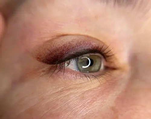 micropigmentacion Primer plano de un ojo verde realzado con sombras marrones y borgoña, delineador negro y arrugas tenues. La iluminación resalta la piel, el maquillaje y los sutiles efectos de la micropigmentación ocular. Monica Aranguez